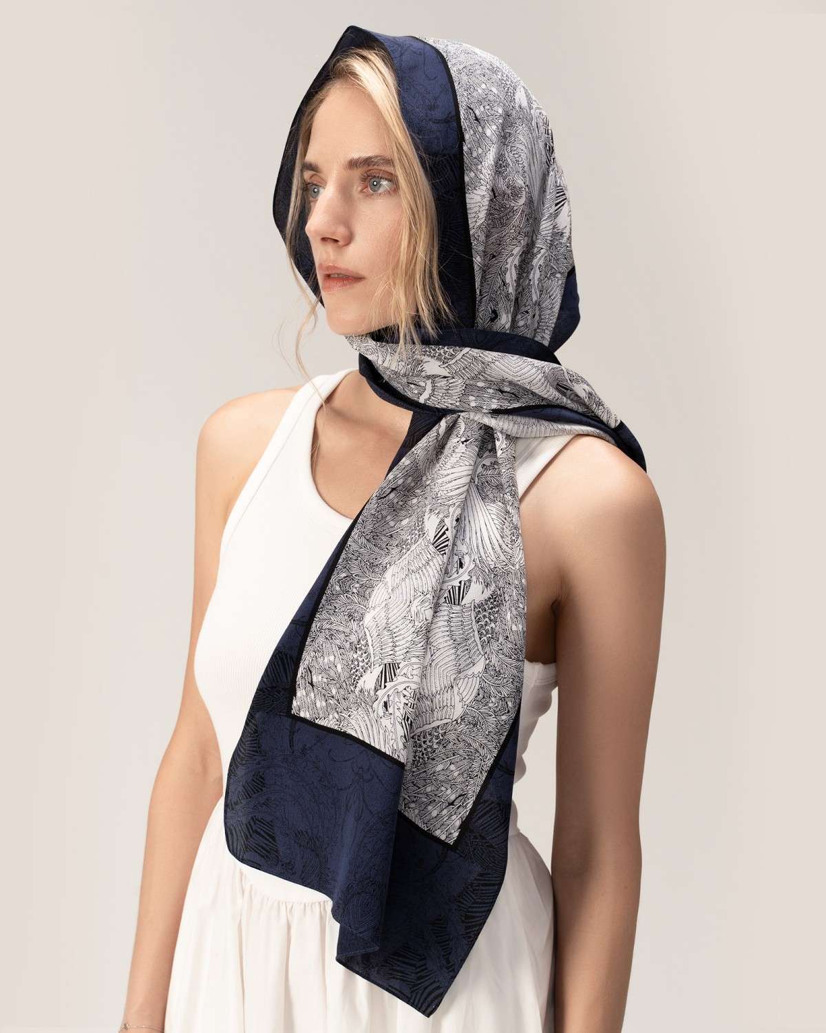 A woman models a white dress, accentuated by a luxurious blue silk head scarf, creating a sophisticated look.