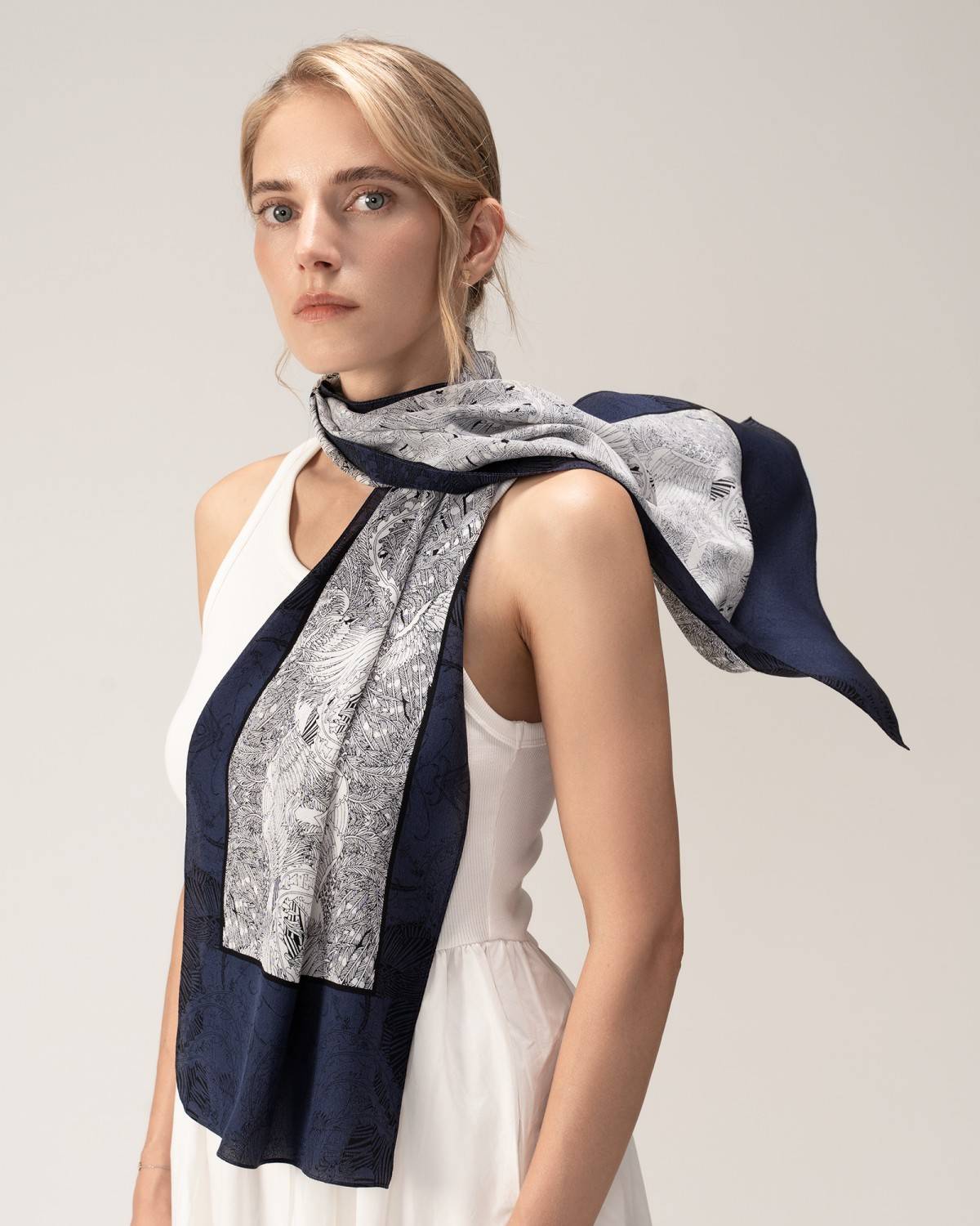 A woman models a rectangular silk scarf featuring a navy and white design, adding sophistication to her outfit.