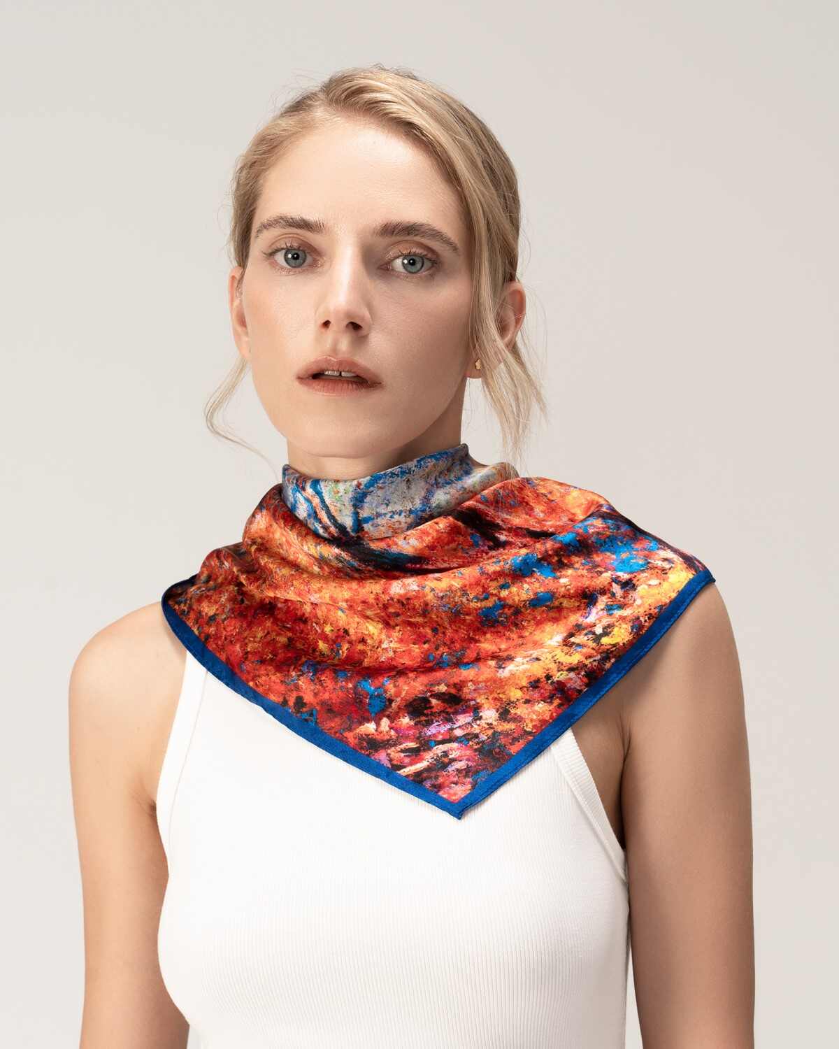 A woman elegantly wears a silk scarf featuring a vibrant orange and blue floral design.