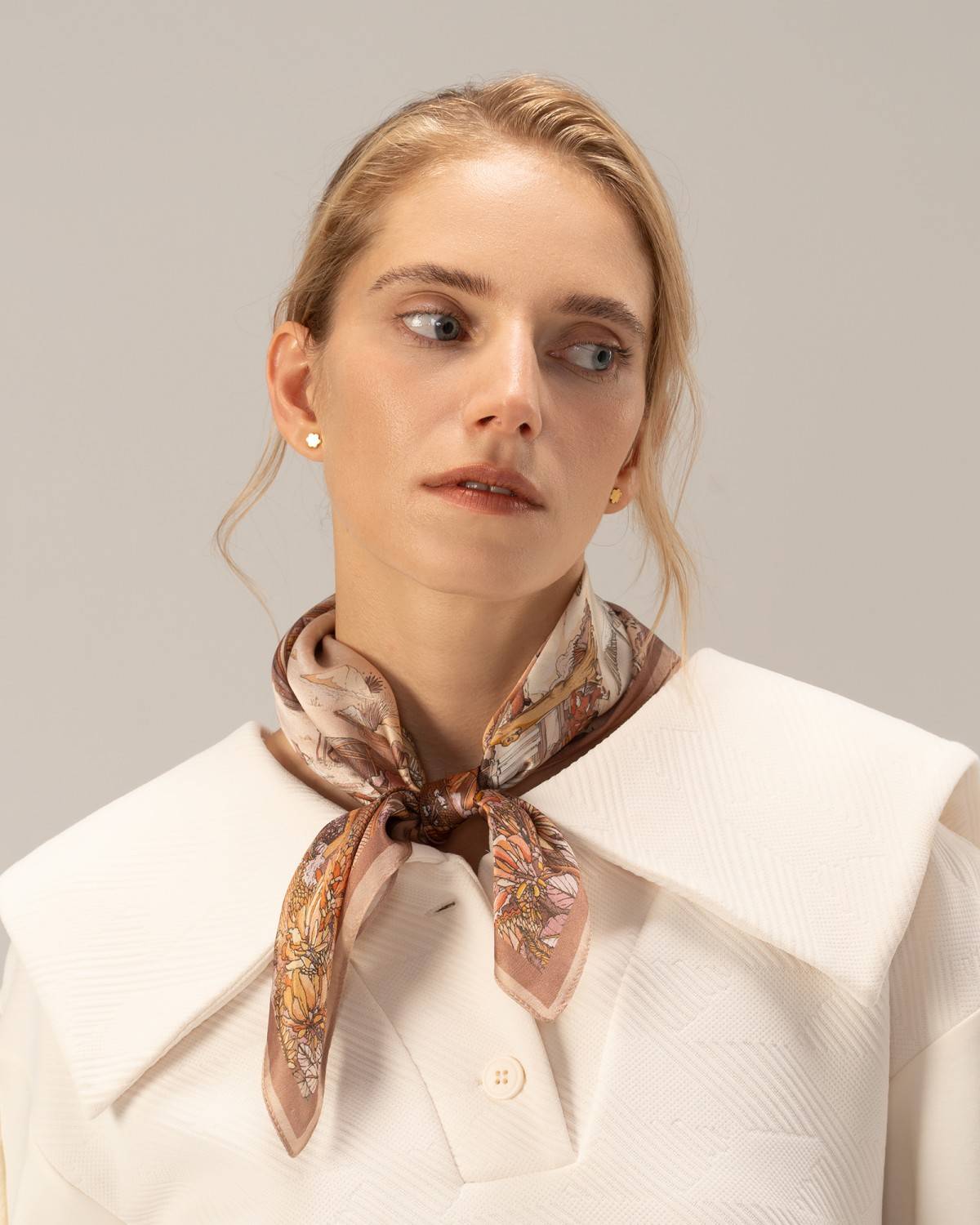 A model wearing a white top and a silk brown scarf adorned with a Chinese painting, showcasing a refined style.